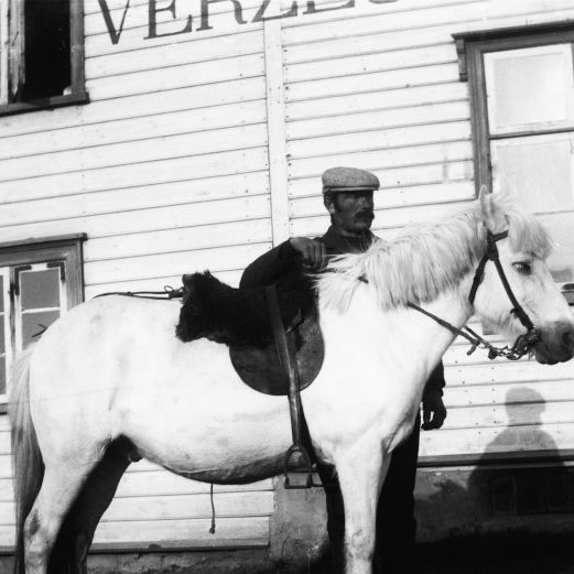 Maður með hest fyrir utan verslun J. A. Jakobssonar. Sést í Kirkjubæ til vinstri.